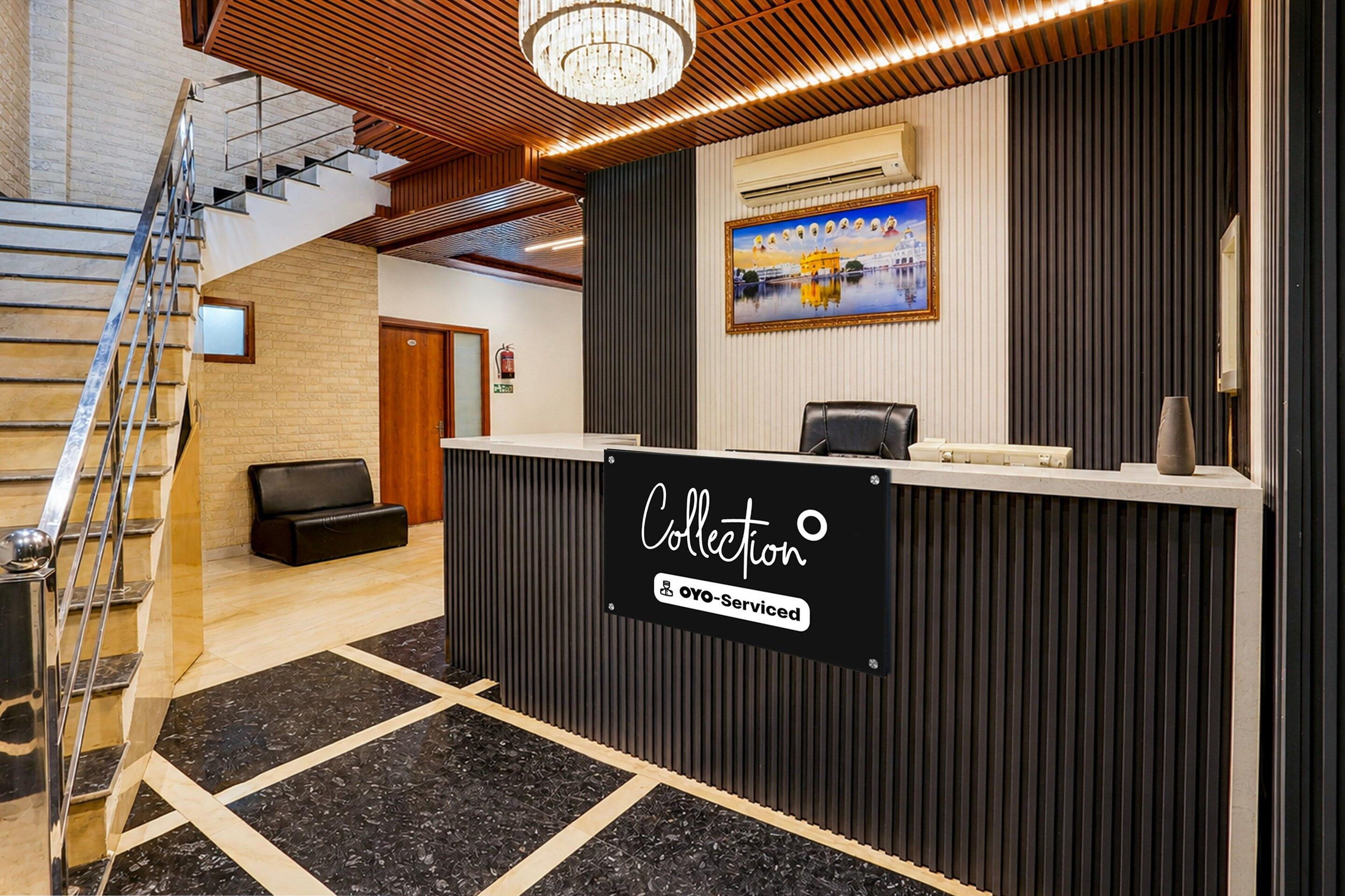 A reception desk with a sign reading 'Collection OYO-Serviced' in a modern interior with a staircase and a framed picture on the wall.