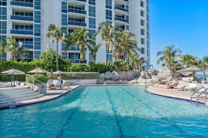 A swimming pool with steps leading into it, surrounded by lounge chairs and umbrellas, with a building in the background. - Navigate Stays Beachfront Pool Resort Sunny Isles (Sunny Isles Beach)