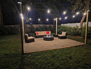 An outdoor seating area with a fire pit, surrounded by a gravel floor and under string lights. - Navigate Stays West Palm Beach 4BR Family Retreat (West Palm Beach)