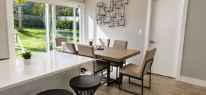A modern kitchen with a large island, a dining area with chairs, and a view of a garden through glass doors. - Navigate Stays West Palm Beach 4BR Family Retreat (West Palm Beach)