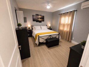 A bedroom with a bed, bedside tables, a ceiling fan, and a window with curtains. - Navigate Stays West Palm Beach 4BR Family Retreat (West Palm Beach)