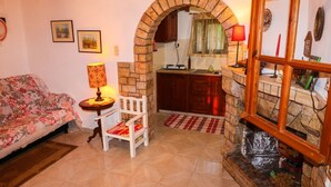 Uma sala de estar com sofá, poltrona, mesa com abajur, lareira e área de cozinha visível por um arco.
