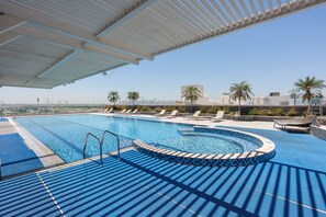 A swimming pool with a curved edge, lounge chairs, and a view of the city skyline. - Free Housekeeping Visits During Your Stay - Stayshort - Stunning Studio in JVT Sleeps 2 With Balcony (Dubai)