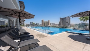 A rooftop pool area with lounge chairs and umbrellas, a clear view of the city skyline, and a swimming pool. - Free Housekeeping Visits During Your Stay - Stayshort - Stunning Studio in JVT Sleeps 2 With Balcony (Dubai)
