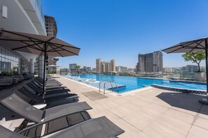 A rooftop pool area with lounge chairs and umbrellas, a clear view of the city skyline, and a swimming pool. - Free Housekeeping Visits During Your Stay - Stayshort - Stunning Studio in JVT Sleeps 2 With Balcony (Dubai)