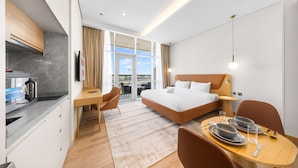 A hotel room with a bed, a desk, a dining table with plates and glasses, a kitchen area, and a view through the window. - Free Housekeeping Visits During Your Stay - Stayshort - Stunning Studio in JVT Sleeps 2 With Balcony (Dubai)