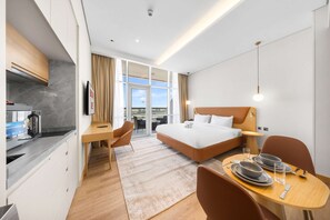 A hotel room with a bed, a desk, a dining table with plates and glasses, a kitchen area, and a view through the window. - Free Housekeeping Visits During Your Stay - Stayshort - Stunning Studio in JVT Sleeps 2 With Balcony (Dubai)