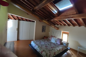 Ein Schlafzimmer mit Holzboden, einem Bett mit Blumenmuster-Bettwäsche, einem weißen Kleiderschrank und einem kleinen Tisch.