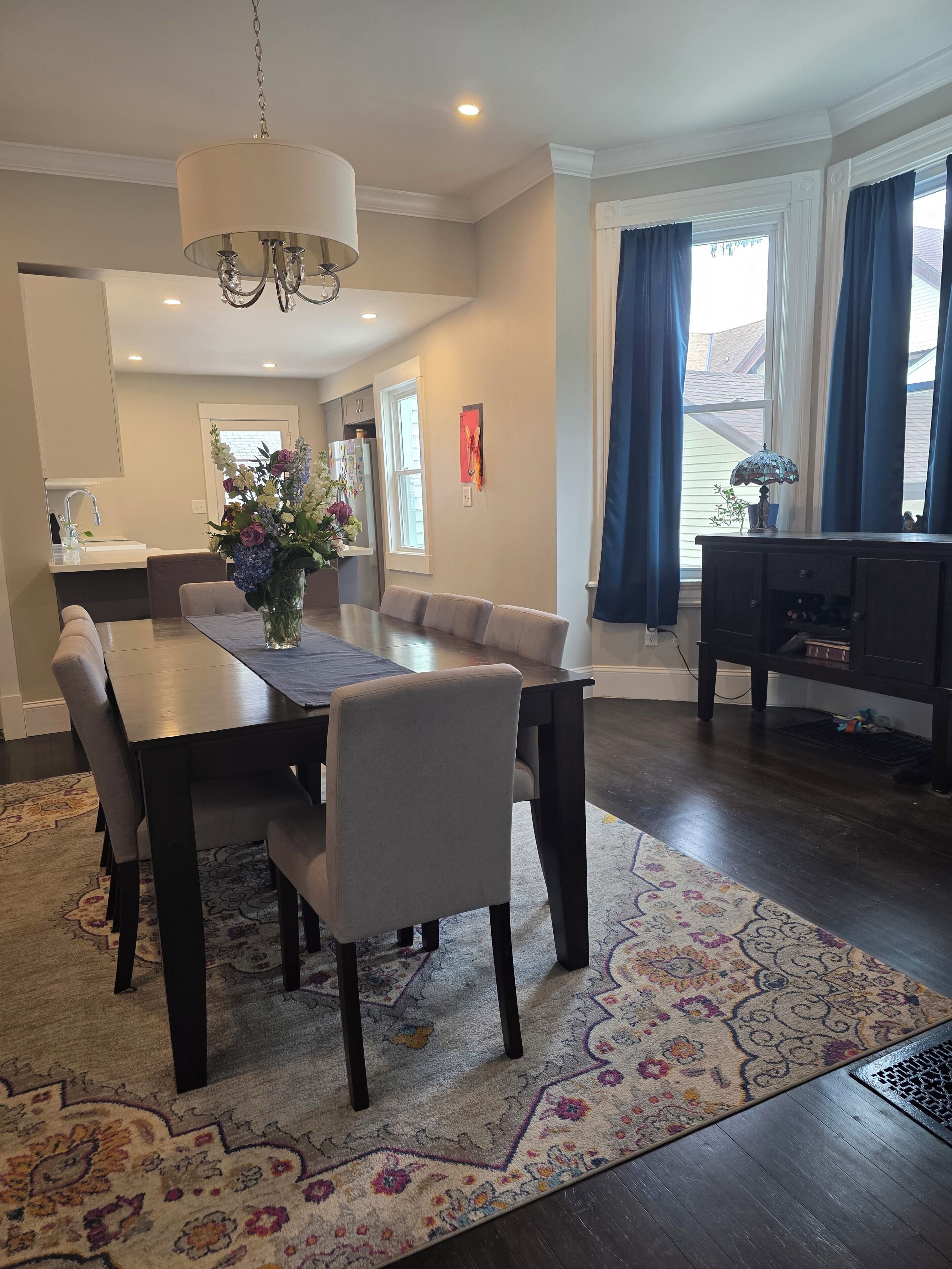 A dining area with a table, chairs, a chandelier, and a rug.