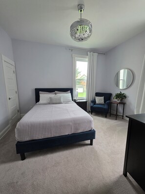 A bedroom with a bed, a bedside table, a chair, a mirror, and a chandelier. - Bright 1 bdrm Norwood apartment near Xavier Factory 52 and Downtown Cincinnati (Cincinnati)