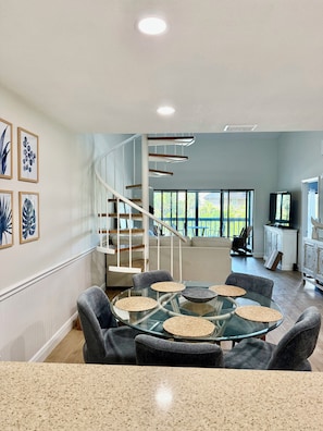 A modern interior with a glass dining table, grey upholstered chairs, a spiral staircase, and large windows. - 3-bedroom condo in charming Siesta Key on intercostal and steps from beach (Siesta Key)