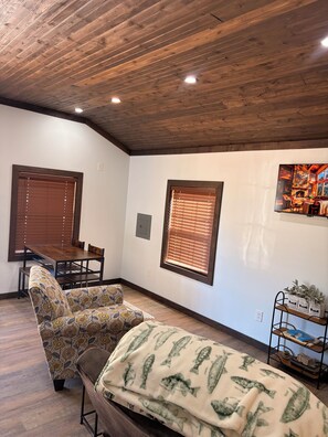 Una habitación con techo de madera, una mesa de comedor con sillas, un sofá, una manta con motivos de peces y un televisor montado en la pared.