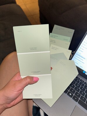 A person holding several color swatches labeled with names and codes, with a laptop in the background. - Peaceful 2-bedroom townhome with AC in charming Tucson (Tucson)