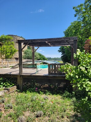 Une terrasse en bois avec une piscine, entourée de verdure et d’un mur de pierres.