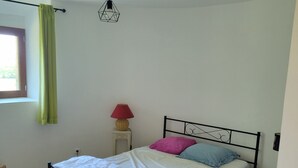 Un dormitorio con cama, lámpara colgante, ventana con cortinas y suelo de madera.