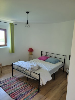 Une chambre à coucher avec un lit, un luminaire suspendu, une fenêtre avec des rideaux et un plancher en bois.