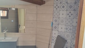 Un baño con lavamanos, espejo, ducha y baldosas estampadas.