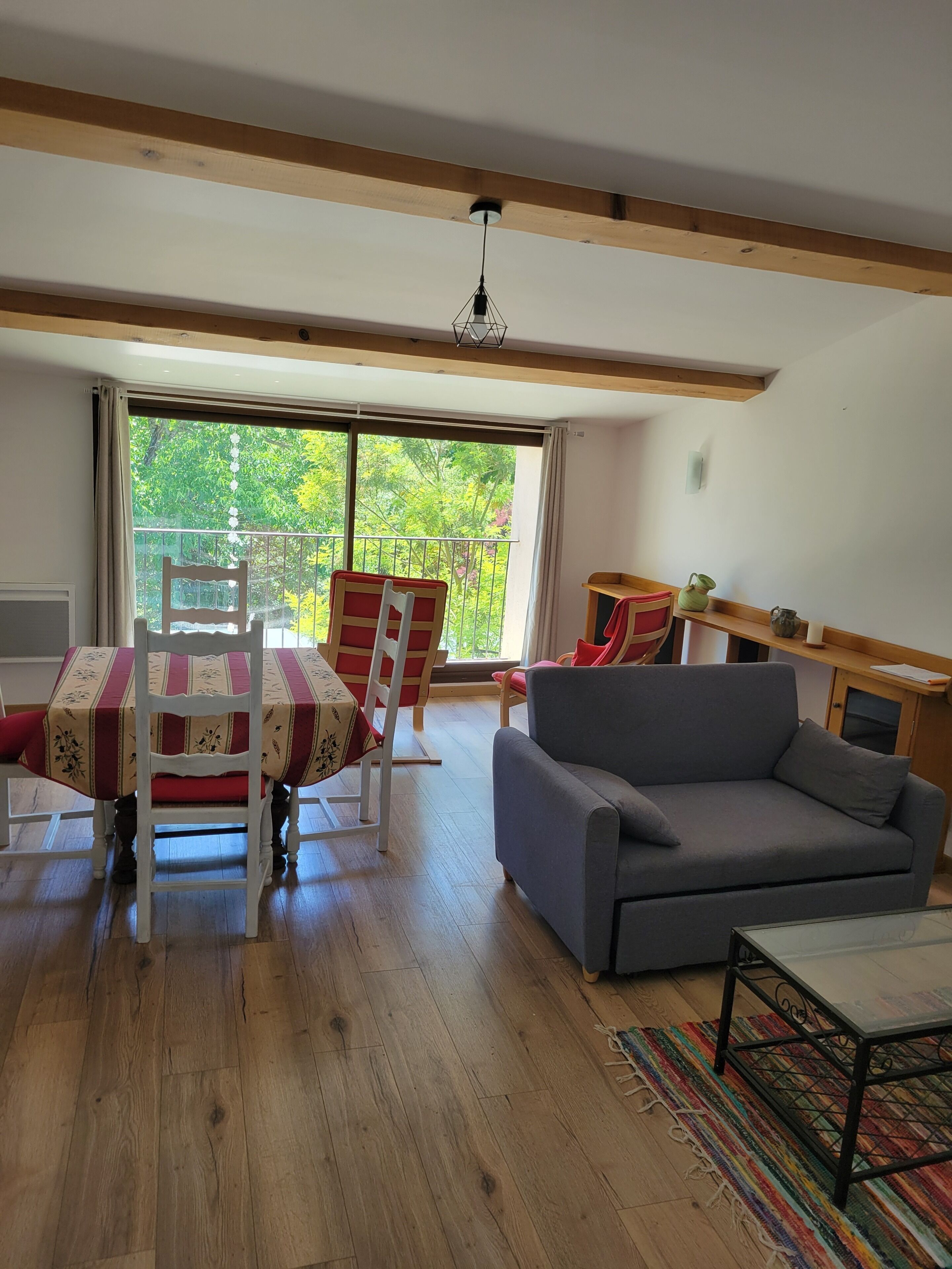 Ein Wohnzimmer mit Esstisch, Stühlen, einer Couch und Blick auf Grünflächen.