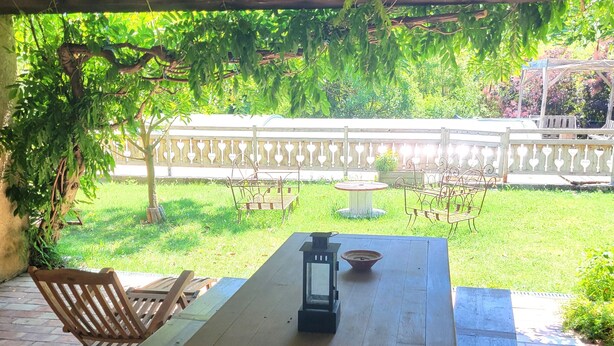 Un patio al aire libre con una mesa de madera, sillas, un farol y piso de ladrillo.