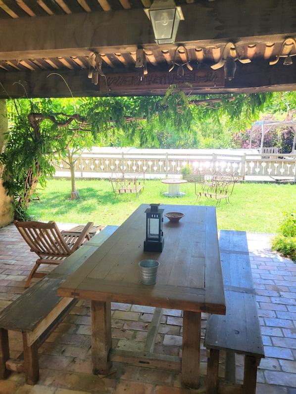 Une terrasse extérieure avec une table en bois, des chaises, une lanterne et un sol en briques.