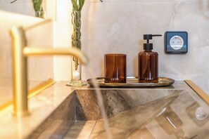 Ein Badezimmer mit Marmorwaschbecken, einer Glasvase mit Pflanze und zwei braunen Flaschen auf einer Ablagefläche.