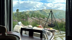 A room with a view of a mountainous landscape, a wooden fence, a hanging light fixture, and a table with a chair. - Charming moutain cabin with charm near Vasstulan (Uvdal)