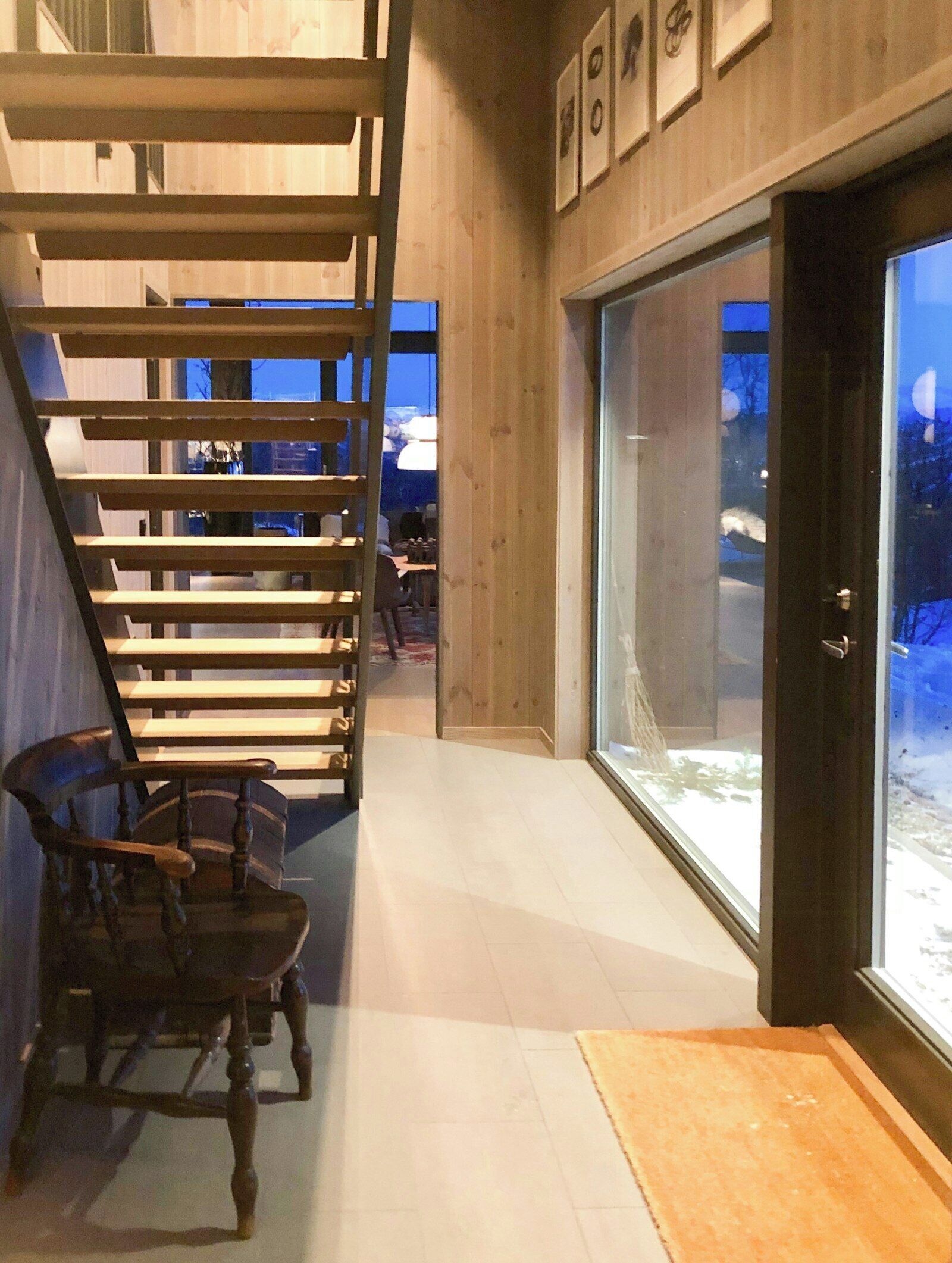 A modern interior with a wooden staircase, a dining area, and a large glass door leading outside.