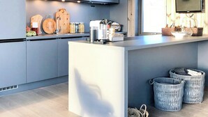 A modern kitchen with grey cabinets, a central island, hanging pendant lights, a TV mounted on the wall, and wicker baskets on the floor. - Charming moutain cabin with charm near Vasstulan (Uvdal)