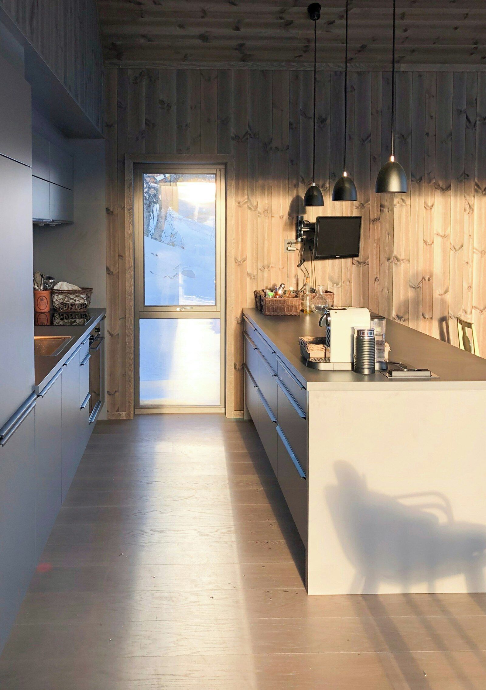 Une cuisine moderne avec des murs en bois, une grande fenêtre et des luminaires suspendus.