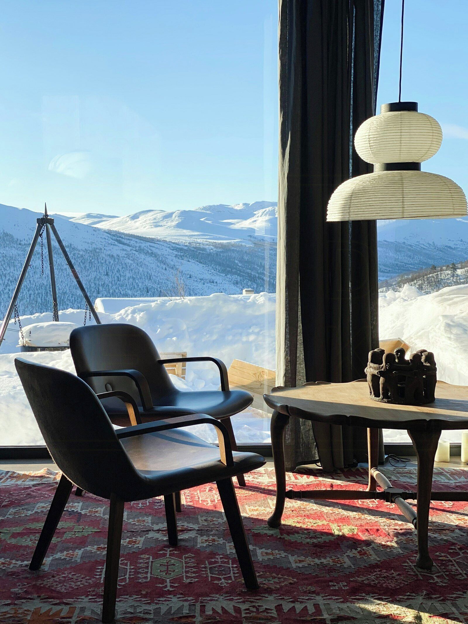 Ein Zimmer mit Blick auf schneebedeckte Berge, einem Stativ, einem Tisch mit einer Lampe und einem Stuhl.