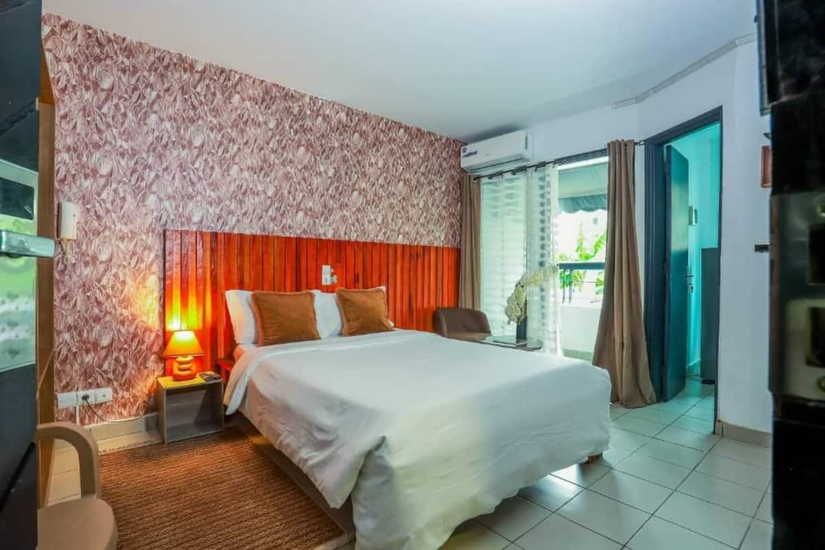Hotellihuone, jossa on sänky, yöpöytä, lamppu, tuoli ja liukuoven kautta avautuva näkymä ulos.