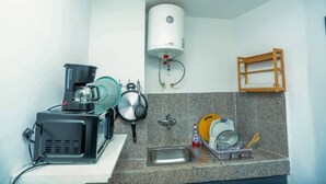 Une cuisine compacte équipée d’une machine à café, d’une bouilloire, d’un évier et d’un égouttoir à vaisselle.