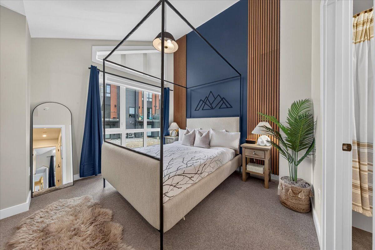 Une chambre à coucher avec un lit à baldaquin, un grand miroir, une plante en pot et une vue sur l’extérieur.