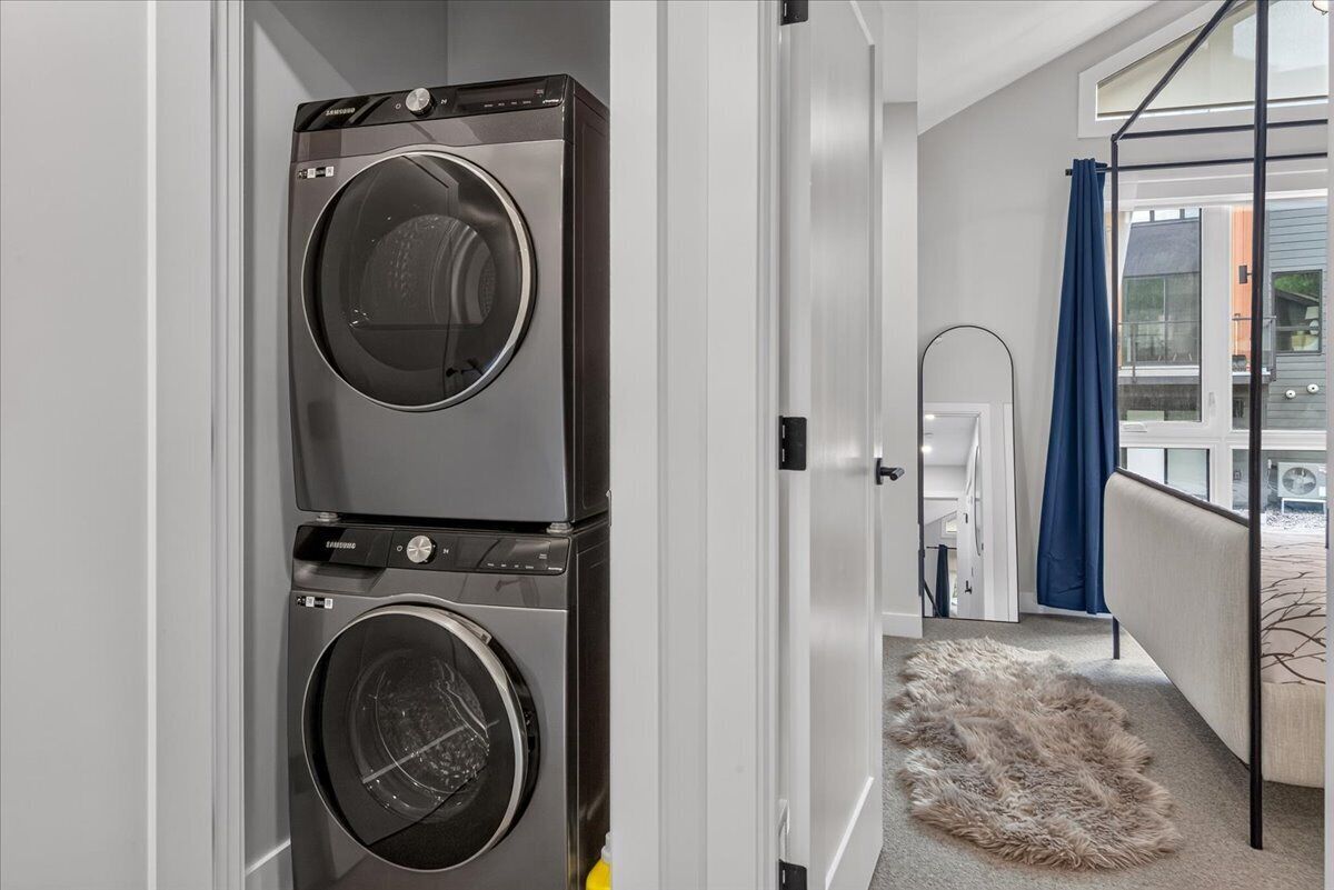 A laundry room with stacked washers and dryers, a white door, and a view of the outside.