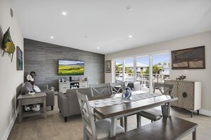 Ein modernes Wohnzimmer mit Fernseher, grauen Sofas, einem Esstisch und einem Balkon mit Blick.