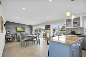 Eine moderne Küche mit einer großen Kochinsel, ein Essbereich mit Ausblick und ein Wohnbereich mit Fernseher.