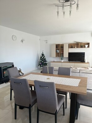 A modern living room with a dining table, grey chairs, a fireplace, a Christmas tree, a TV, and built-in shelves.