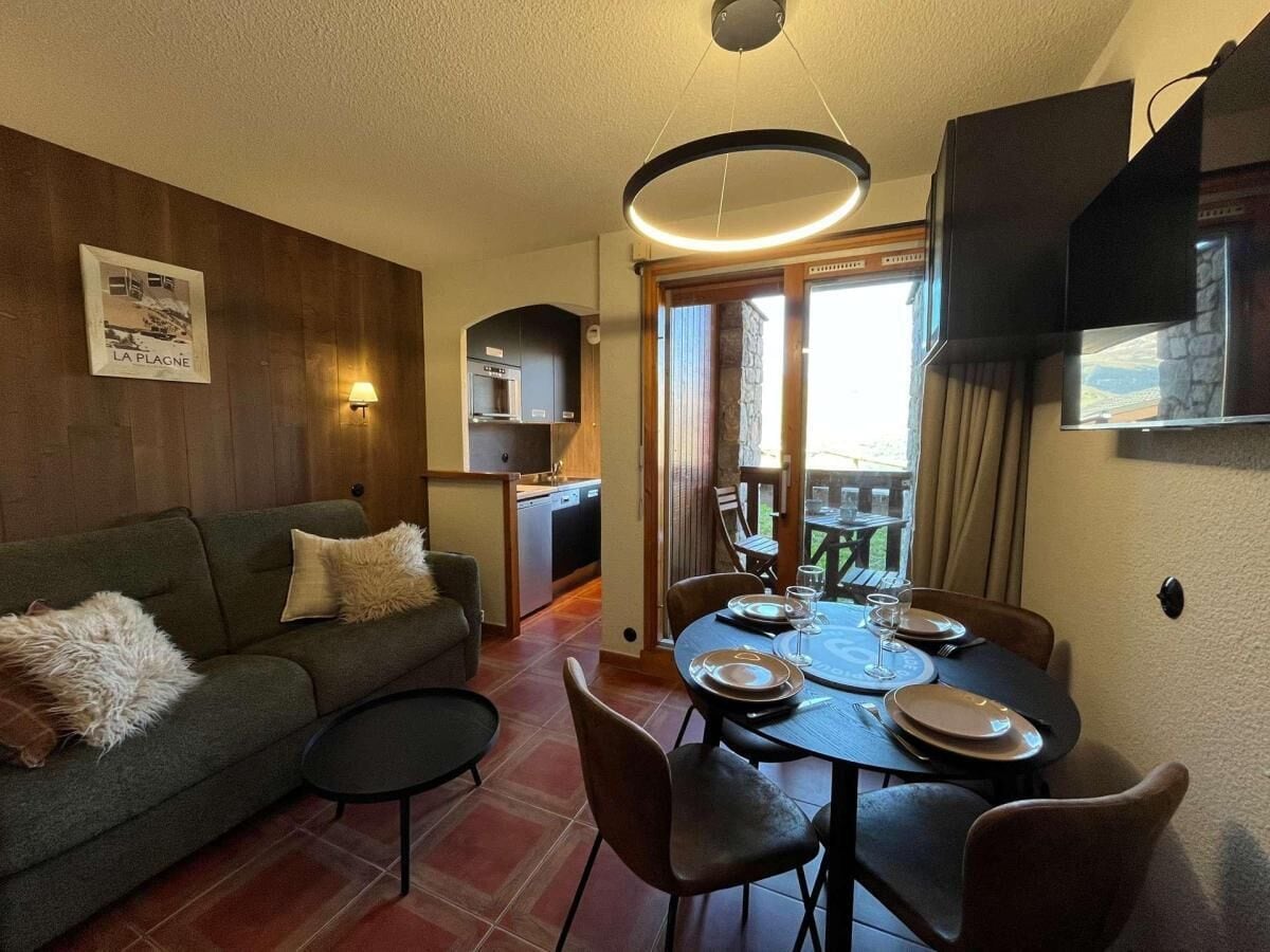 Un salon confortable avec un canapé, une table à manger dressée pour quatre personnes et une cuisine en arrière-plan.