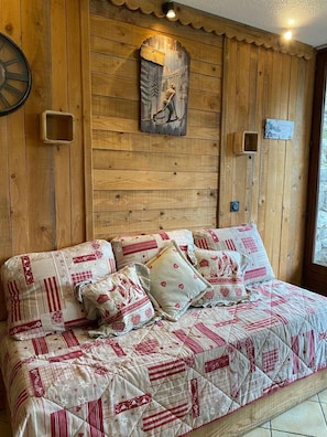 Interior de cabana de madeira com cama, almofadas, relógio de parede e porta de madeira.