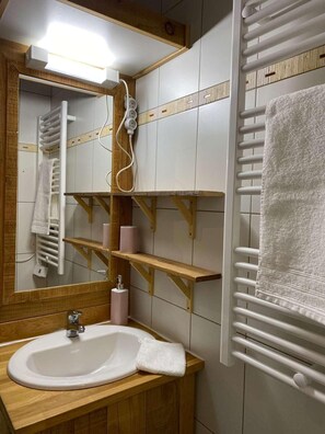 Ein Badezimmer mit einem weißen Waschbecken, Holzregalen, einem Spiegel und einem Handtuchhalter.