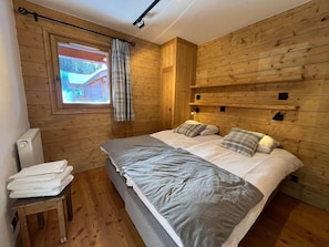 A wooden-paneled room with a bed, a window with a view, a radiator, and a small table with towels. - Up to 10 meters from the ski slope, 2nd floor, terrace, parking, TV, 80 m², Peisey-Vallandry (Landry)