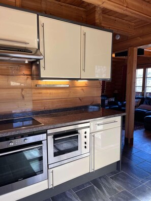 Een moderne keuken met inbouwapparatuur, een houten plafond en uitzicht op de woonkamer.