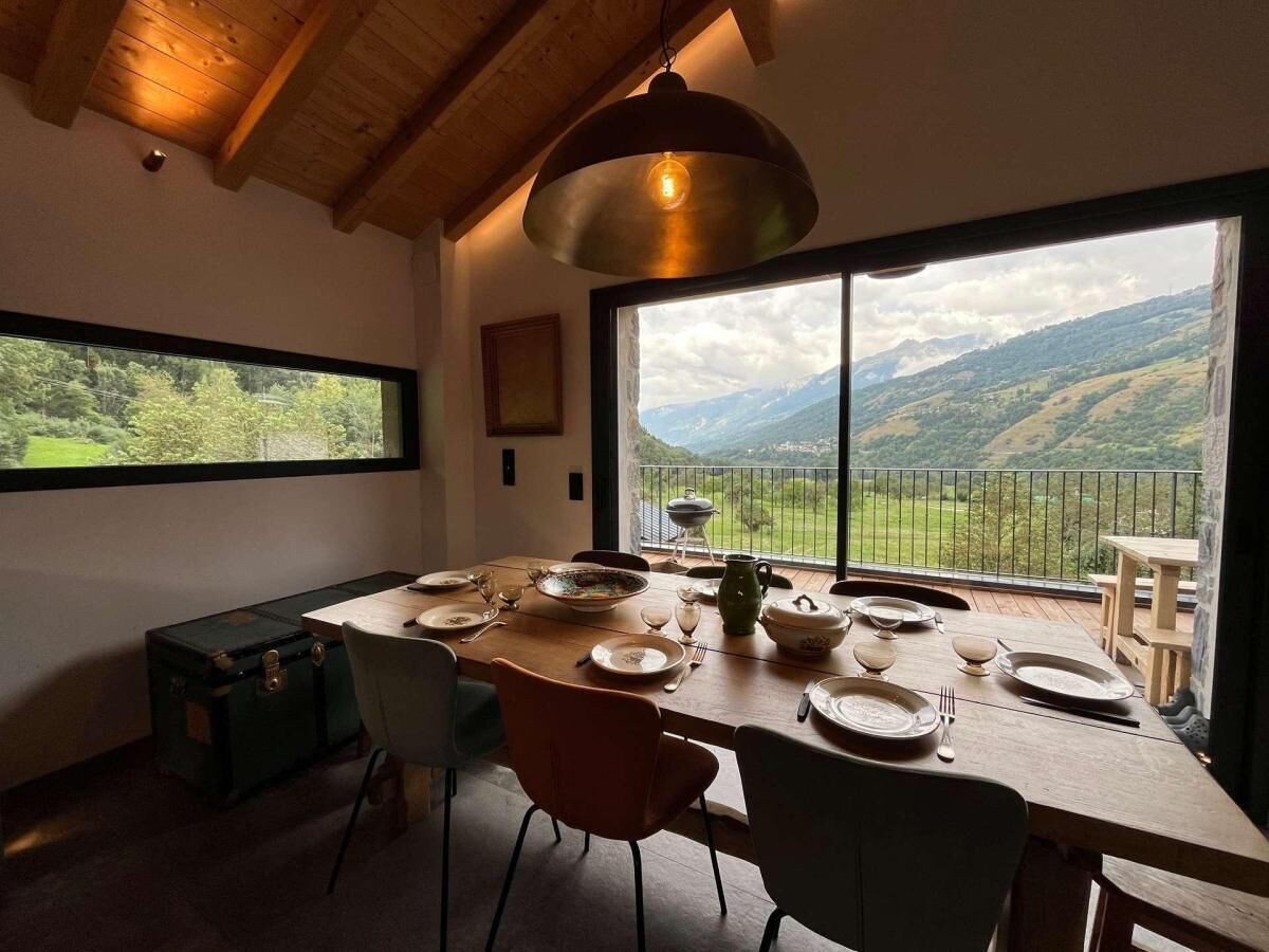 A dining area with a table set for four, a large window with a view of a mountainous landscape, and a hanging light fixture.