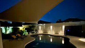 Piscina com borda curva, rodeada por espreguiçadeiras e uma área coberta.
