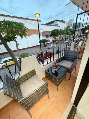 Ein Balkon mit Korbmöbeln, einem kleinen Tisch und Blick auf die Straße.
