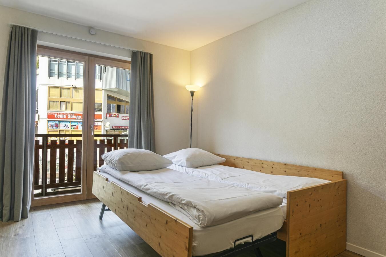 A single bed with a wooden frame and white bedding in a room with a balcony.