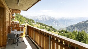 Een houten balkon met een tafel en stoelen, met uitzicht op een bergachtig landschap.
