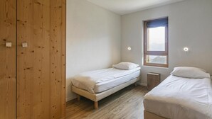 Een slaapkamer met twee enkele bedden, een houten garderobe, een raam met uitzicht en inbouwspots.