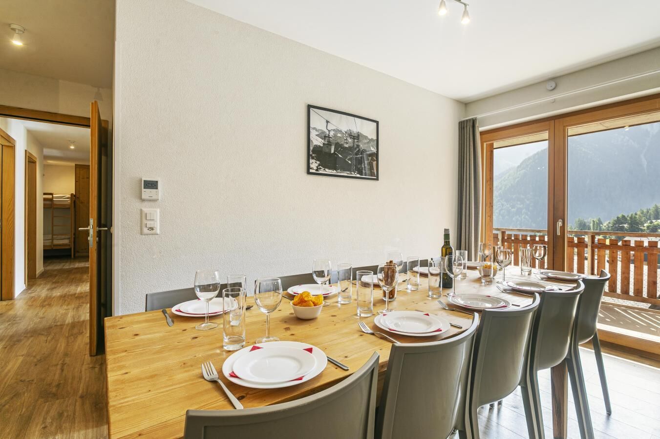 A dining room with a wooden table set for six, chairs, and a view of mountains through large windows.