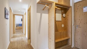 Un couloir doté d’un plancher en bois, une porte en bois avec un porte-manteau suspendu, et une vue sur une pièce avec un lit et un mur bleu.